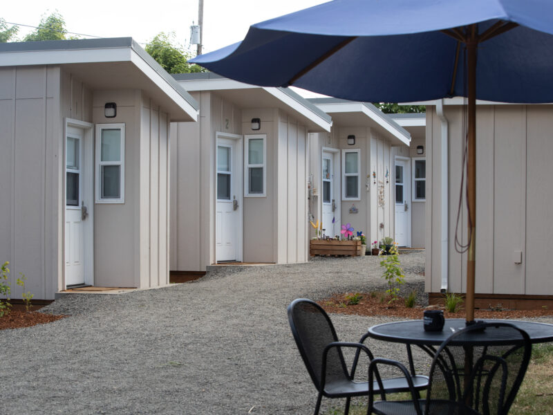 A row of tiny homes on a gravel path, with a large umbrella in the foreground.
